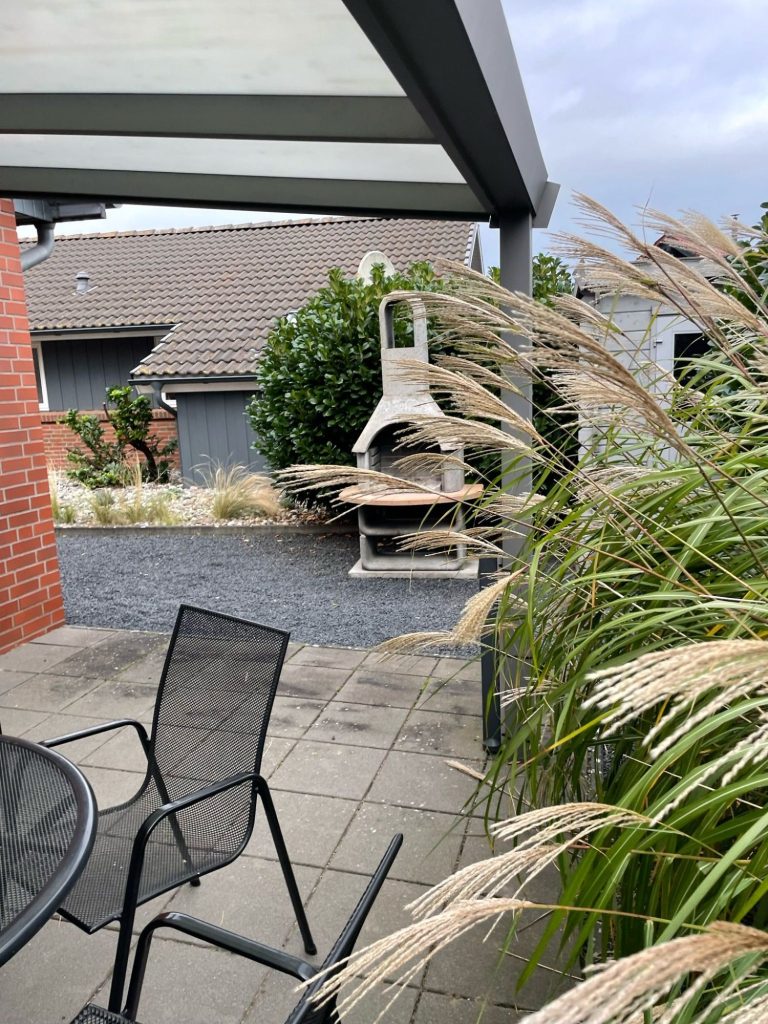 Terrasse mit Tisch, Stühlen und Überdachung, umgeben von grüner Rasenfläche.