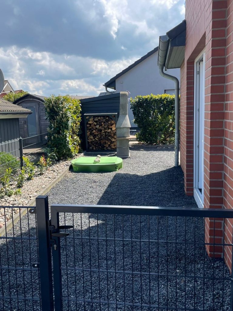 Terrasse mit Tisch, Stühlen und Überdachung, umgeben von grüner Rasenfläche.
