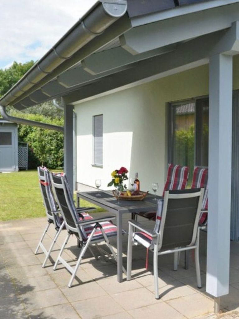 Terrasse mit Tisch, Stühlen und Überdachung, umgeben von grüner Rasenfläche.